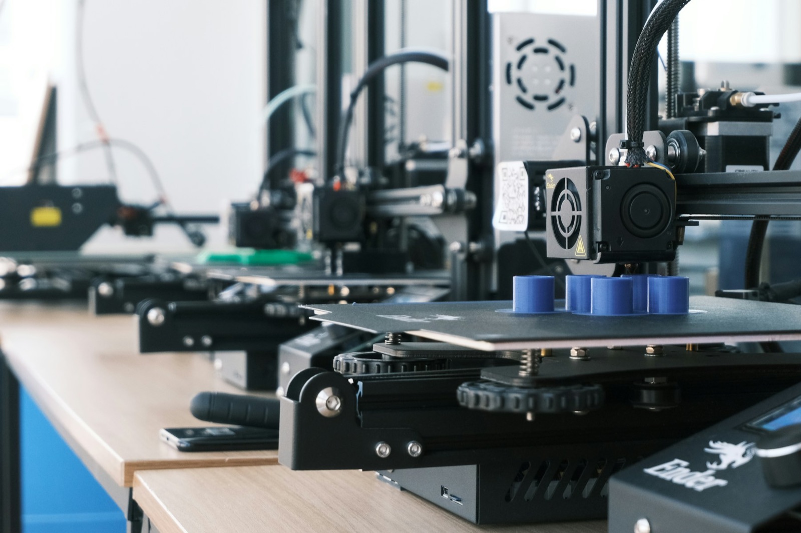 A row of 3D printers running a small series of blue parts